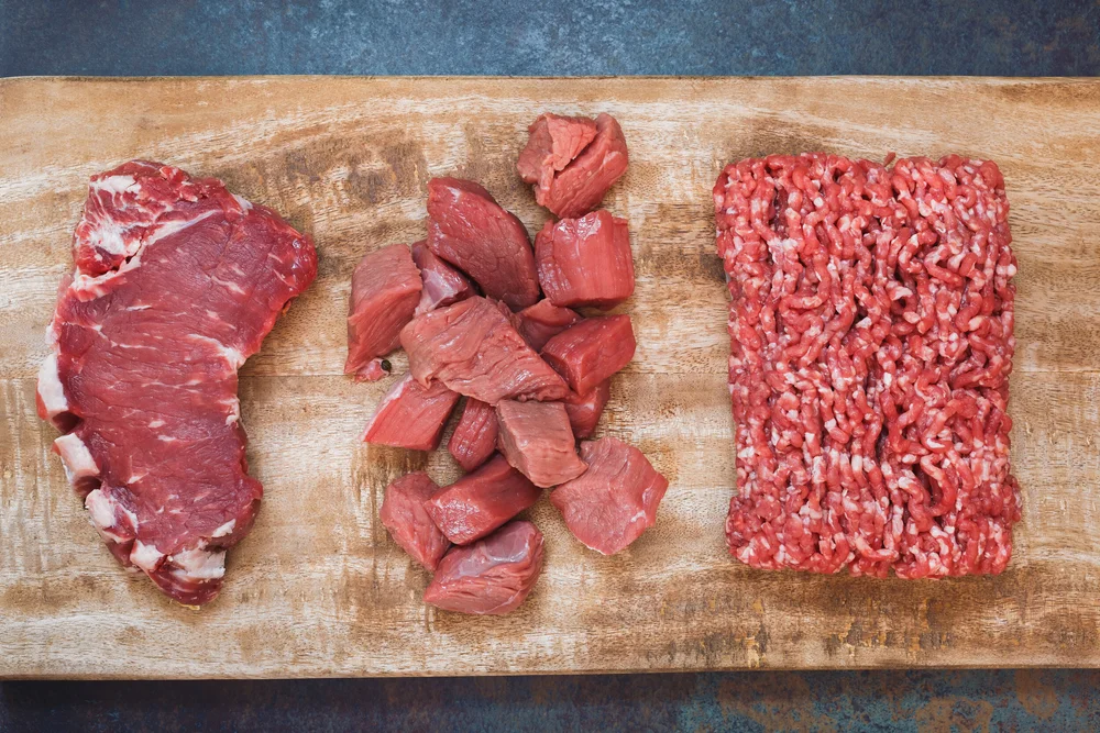 Beef+Mix+Cuts Assorted cuts of beef including a ribeye steak, diced beef chunks, and ground beef on a wooden cutting board, showcasing fresh meat options for cooking and meal preparation.
