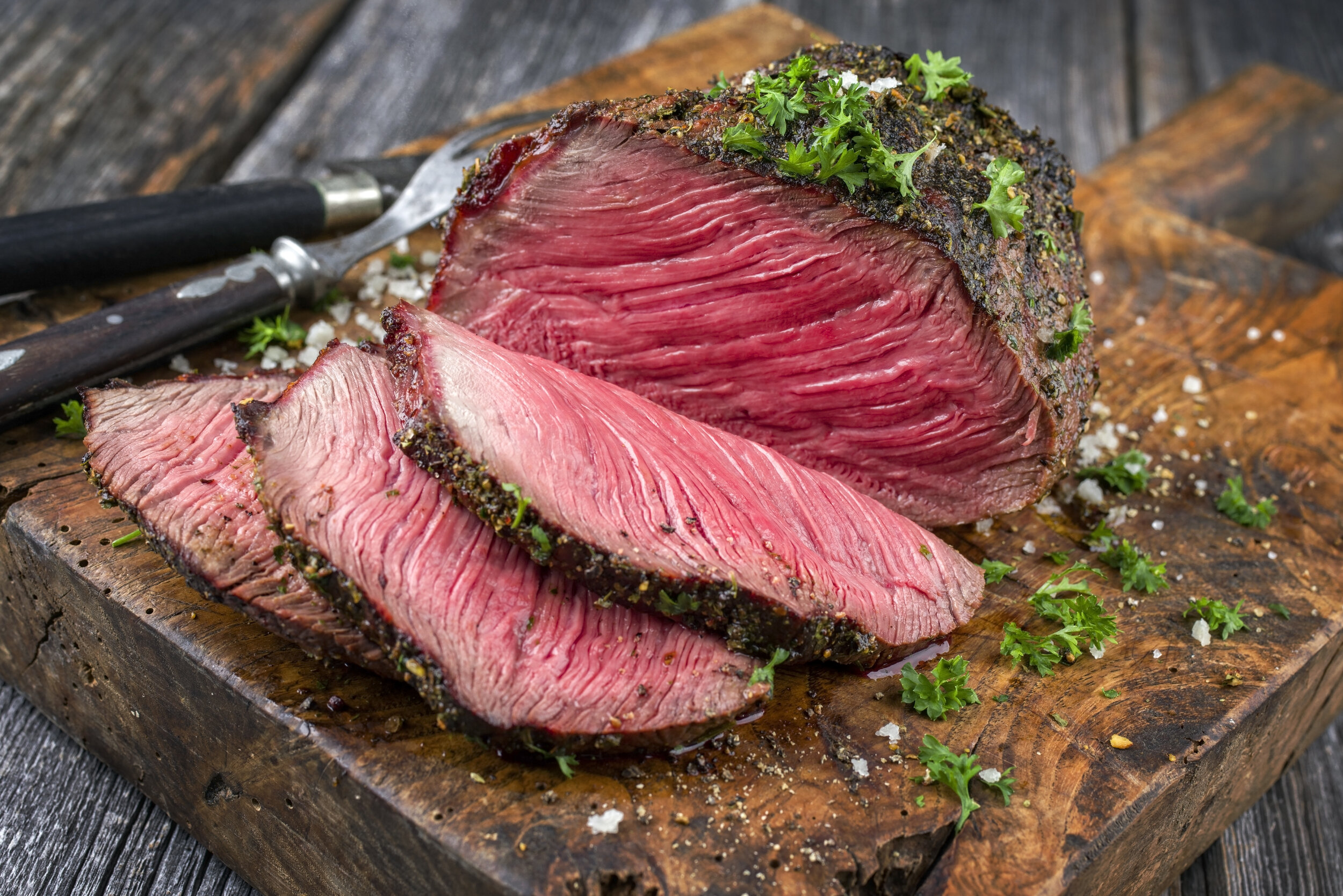 Barbecue wagyu point steak sliced as close-up on a cutting board Sliced roast beef with a seasoned crust, garnished with fresh parsley, displayed on a rustic wooden cutting board, showcasing its tender, juicy texture.