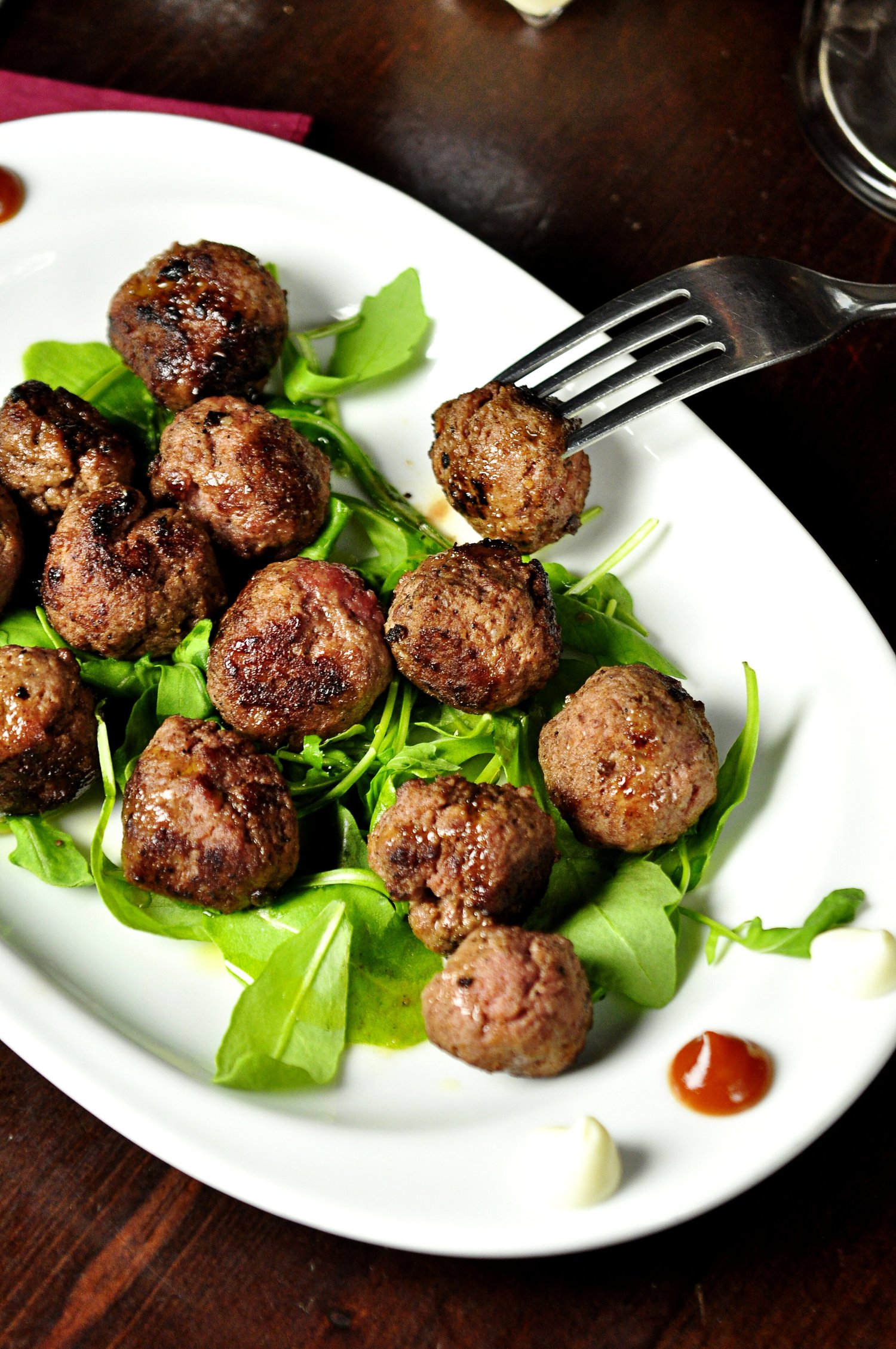 image-asset (6) Plate of juicy meatballs served on a bed of fresh arugula, garnished with sauces, showcasing a delicious appetizer or main dish option.