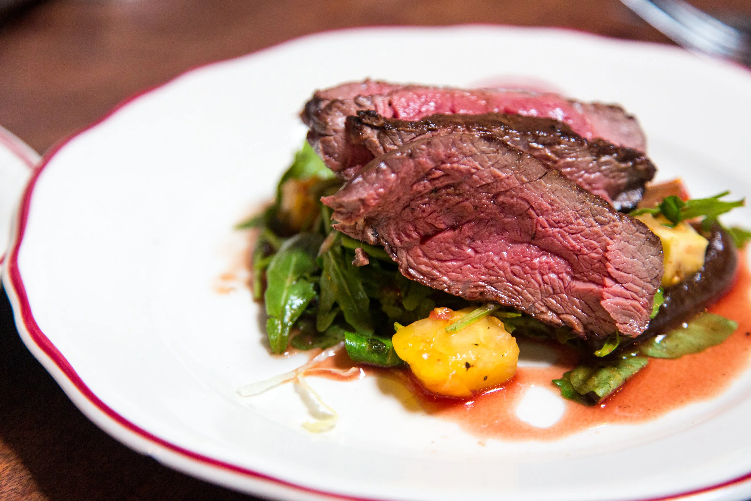 image-asset Juicy slices of medium-rare beef served on a bed of fresh greens and garnished with vibrant pineapple pieces, creating a delicious and visually appealing dish.